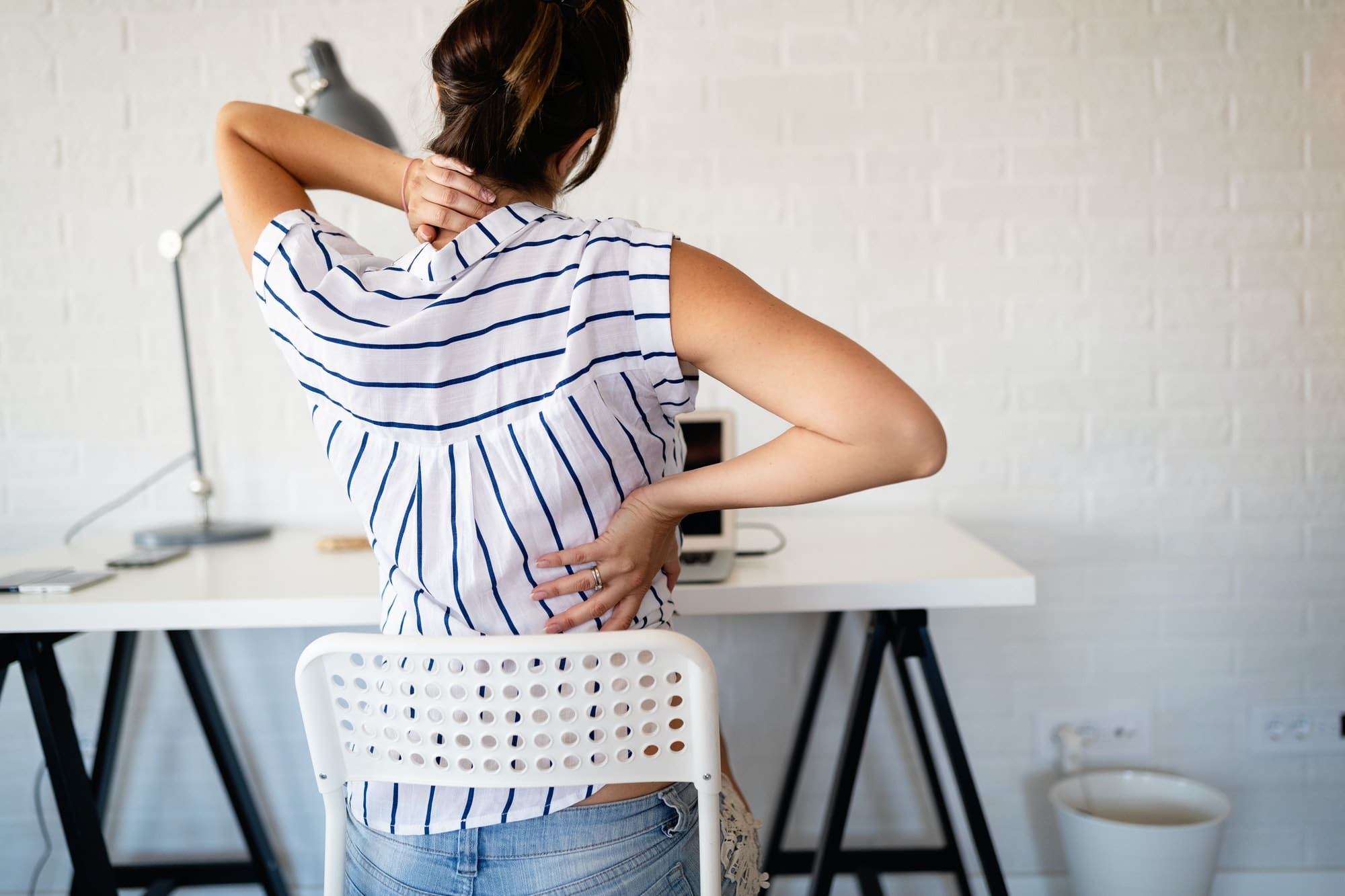 Overworked woman with back pain in office with bad posture